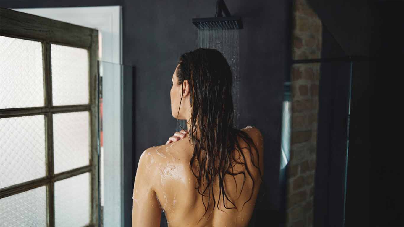 Vrouw staat onder de douche met haar rug naar ons gekeerd